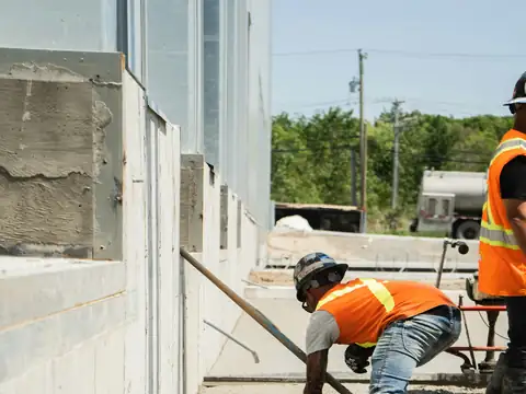 Construction worker in a high-visibility vest finishing a freshly poured concrete slab, face not shown