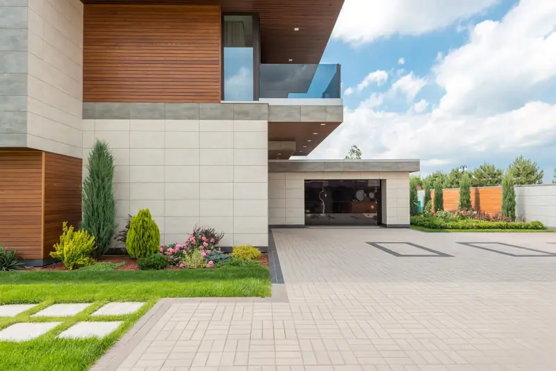 Herringbone-pattern paver driveway and walkway leading to a modern house garage with landscaped planting beds