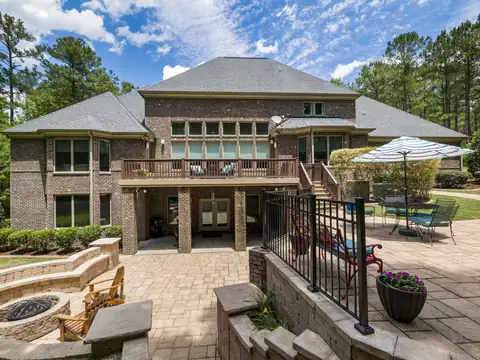 Paver patio behind a brick house with a stone fire pit, wooden chairs, umbrella table, and wicker furniture