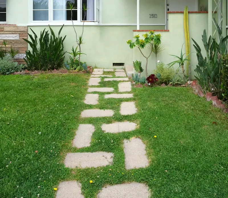 Concrete paver stepping-stone path crossing a green front lawn toward a house entrance with landscaping